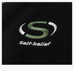 Detailed close-up of high-quality green S embroidery and Self-belief text on black fabric
