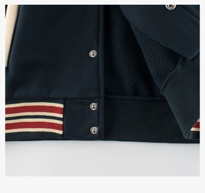 Detail of navy fleece-lined baseball jacket with metal snaps and striped ribbed hem