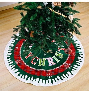 Detail of red and green Christmas tree skirt with Merry Christmas lettering on wood floor