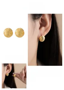 Detail showing the matte brushed texture and golden pleated design of circular stud earrings