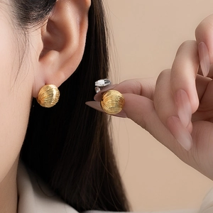 Golden pleated round stud earrings with spiral texture shown on ear and held by hand