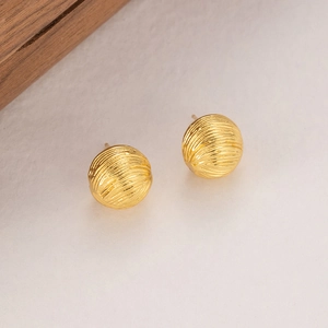 Detailed macro view of gold-plated spherical earrings featuring a textured wavy pattern