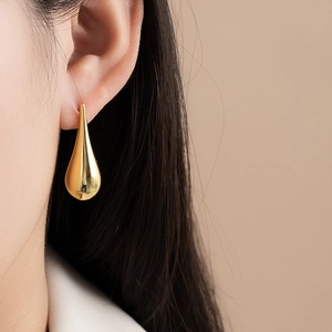 Detailed close-up of a large gold waterdrop earring with a high-polished mirror finish