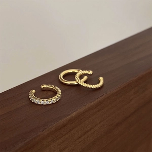 Three-piece gold ear cuff set with smooth, twisted, and pavé diamond designs on wood
