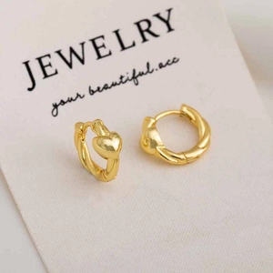 Detailed view of gold twisted hoop earrings with polished heart charms on a display card