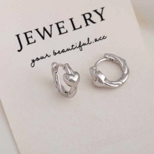 Close-up of silver-tone twisted hoop earrings with a smooth heart-shaped pendant