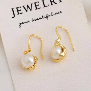 Macro shot of irregular gold earrings with white pearl detail on minimalist jewelry card
