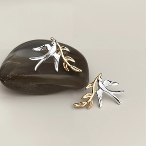Two-tone swallow bird stud earrings with golden olive branch on smooth pebble stone