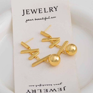 Détail de boucles d'oreilles dorées avec barres longues et sphères sur carte bijou