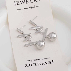 Détail de boucles d'oreilles boules à pompon argentées avec forme en X géométrique