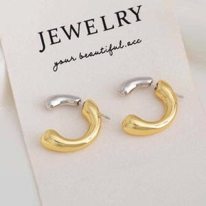 Macro detail of two-tone gold and silver C-shaped teardrop earrings on a jewelry card