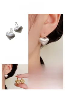 Detail of brushed heart-shaped hoop earrings in gold and silver showing clasp mechanism