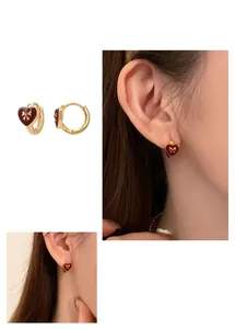 Detail of heart-shaped earrings with red oil drip finish and golden bow decoration