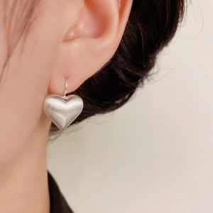 Brushed heart-shaped drop earrings in matte silver finish shown on a model's ear