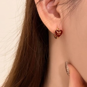 Elegant heart earrings with red enamel and gold bow detail on a model