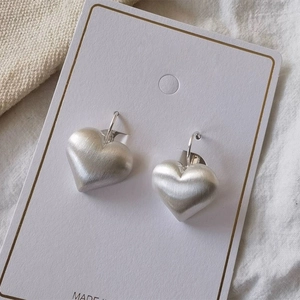 Close-up of matte silver heart earrings with a brushed metal texture on a white display card