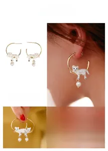 Détail de boucles d'oreilles chat et perle en émail blanc avec finition dorée