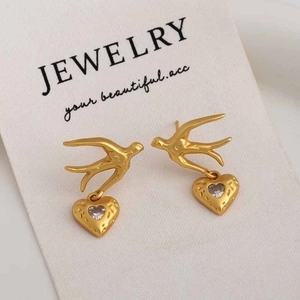 Macro shot of gold bird earrings with heart zircon pendants on a jewelry card