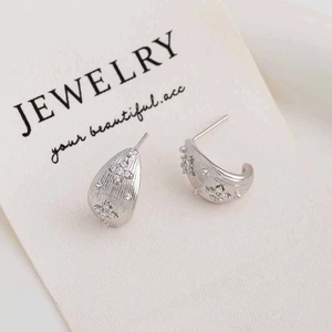 Macro shot of silver C-shaped earrings with brushed metal finish and zircon clover detail