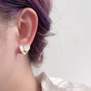 Détail des boucles d'oreilles en forme de cœur en émail blanc et finition dorée