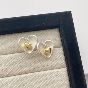 Détail de boucles d'oreilles cœur argent mat avec pendentif cœur 3D doré sur lin beige