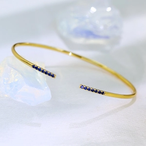 Detail of adjustable open cuff bracelet featuring rows of blue cubic zirconia on gold metal