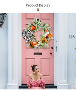 Detail of autumn wreath with cotton, pumpkins, and black-white plaid bow on a pink door