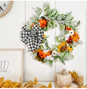 Detail of autumn wreath with pumpkins, cotton and buffalo plaid bow on white wood wall
