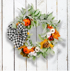 Detail of autumn wreath with mini pumpkins, pine cones, and a plaid bow on white wood