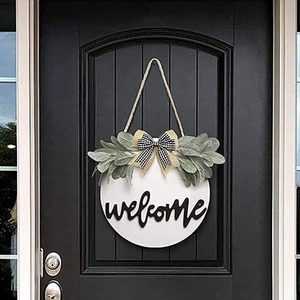 White wooden welcome sign with green foliage and rustic bow hanging on a black door