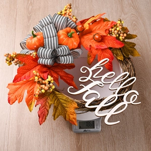 Detail shot of Hello Fall wreath with pumpkins and maple leaves on a weighing scale