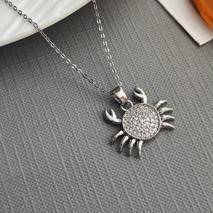 Collier avec pendentif crabe en argent et oxydes de zirconium sur fond texturé gris