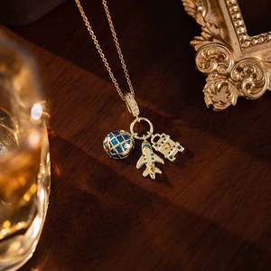 Vue détaillée du pendentif avion doré, globe en émail bleu et étiquette avec zircons