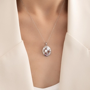 Detailed view of silver oval pendant with pink stones and pearl on a model neckline