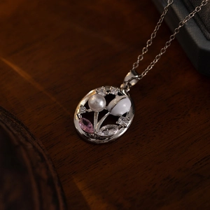 Macro detail of oval titanium steel necklace with pink zircon flower and pearl inlay