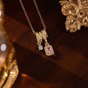 Close-up of a gold necklace featuring a pink rectangle crystal and sparkling zircon accents