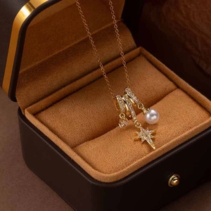 Detail of gold star pendant necklace with pearl and zircon charms in jewelry box