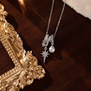 Detail of star pendant necklace with micro-pave crystals and a white pearl on wood