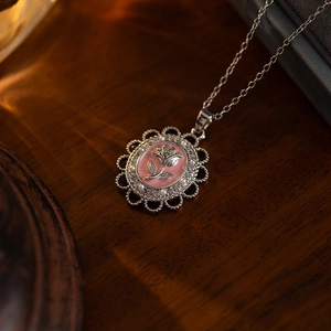 Macro shot of rose relief pendant with pink enamel and intricate silver lace detail