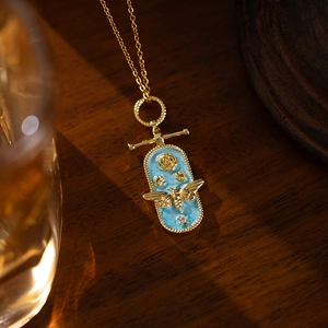 Macro shot of vintage gold bee necklace with blue enamel pendant and rose detail