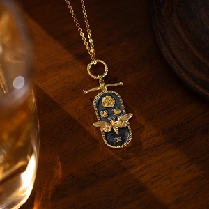 Macro detail of a vintage gold bee necklace with black enamel and a small white gemstone