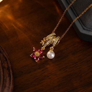 Macro detail of gold flower pendant necklace with red zircon, pearl and pavé ring elements