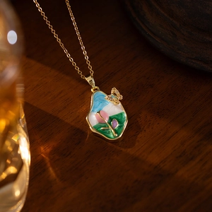 Detail view of a gold flower necklace with pink tulip enamel pendant and butterfly charm
