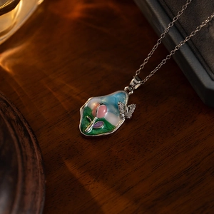 Detail of tulip flower enamel pendant with butterfly accent on rustic wood table