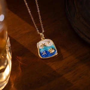Dreamy blue ocean enamel necklace with gold starfish and seashell pendant on a wood background