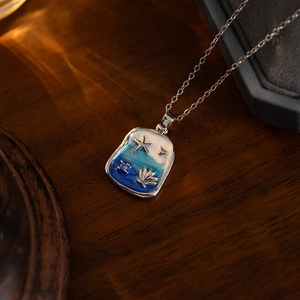 Blue ocean enamel necklace with silver starfish and shell pendant on wood background