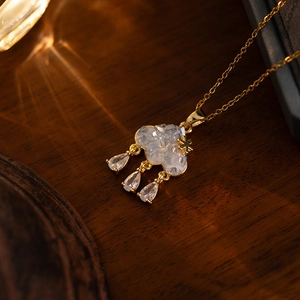 Macro detail of gold cloud pendant with zircon tassels on a dark wood background