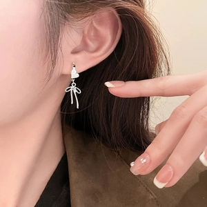 Detail of silver heart and bow earrings with sparkling stones on a model's ear