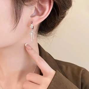 Detail of silver heart bow earrings with micro diamonds worn on model for scale
