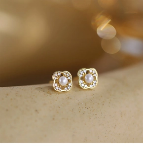 Detailed close-up of golden four-leaf clover stud earrings with pearls and crystals